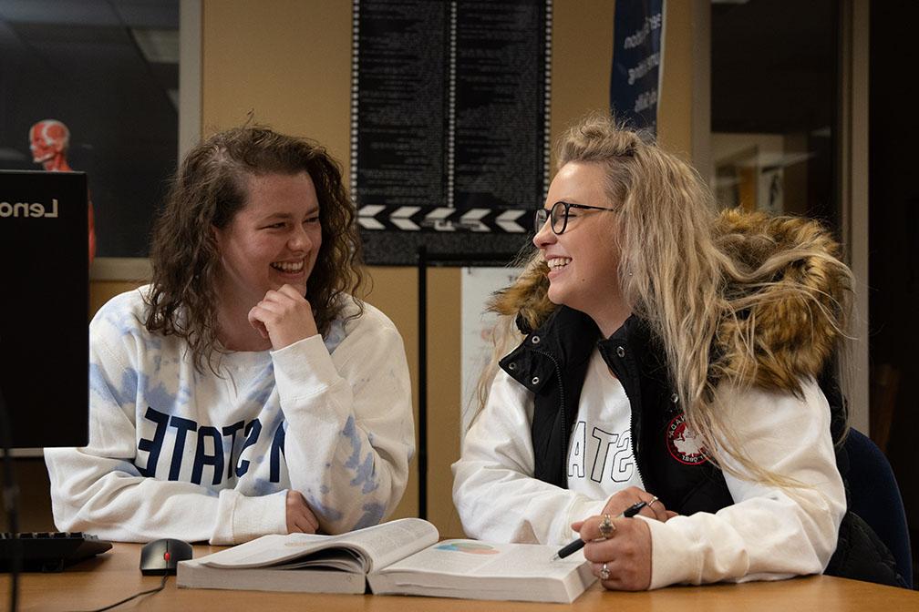 Two students seated at a table, laughing